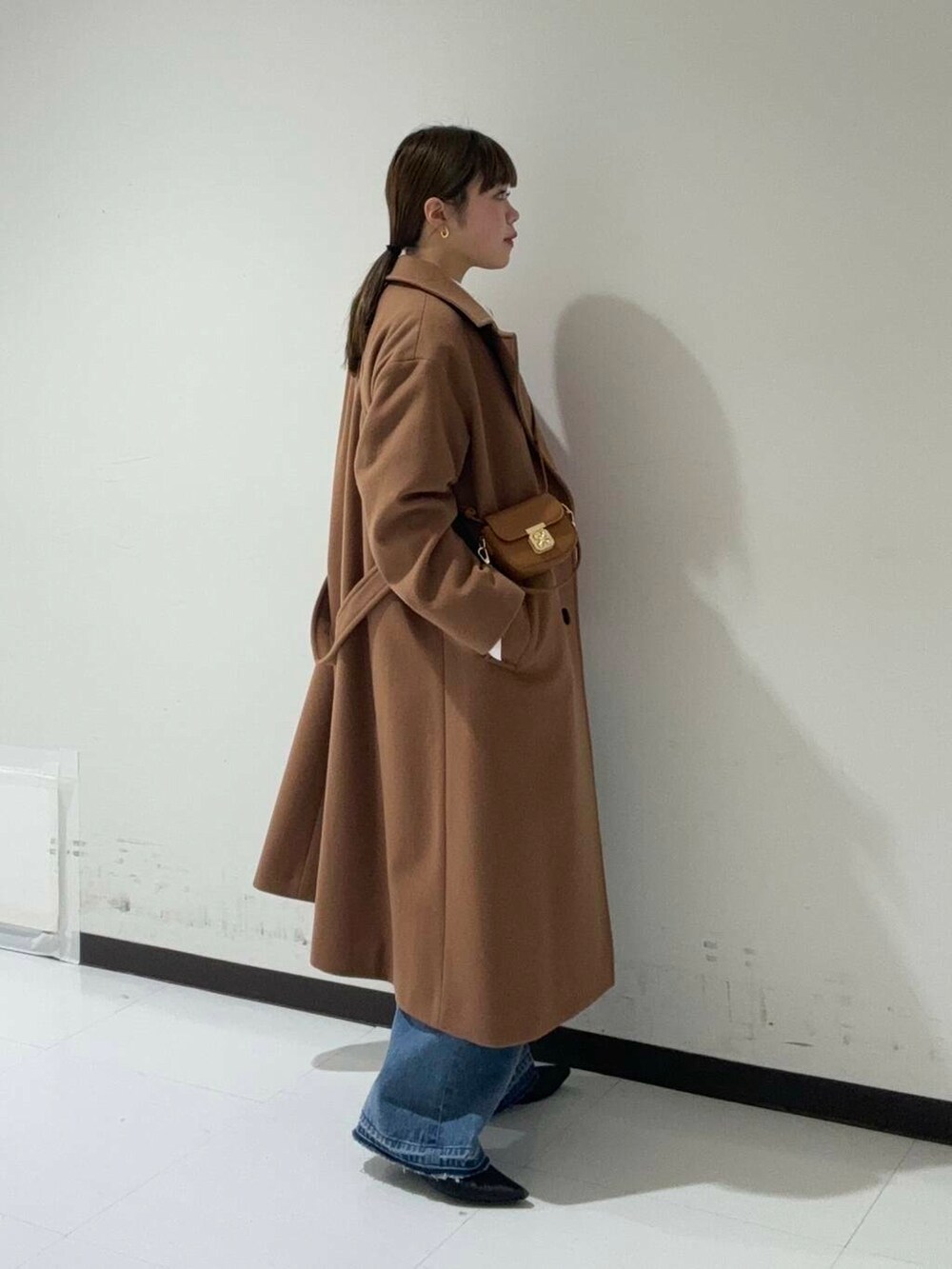 イエロー系のチェスターコート、ブルー系のデニムパンツ、レッド系のニット/セーターを着用したレディースの冬コーディネートの2枚目の写真