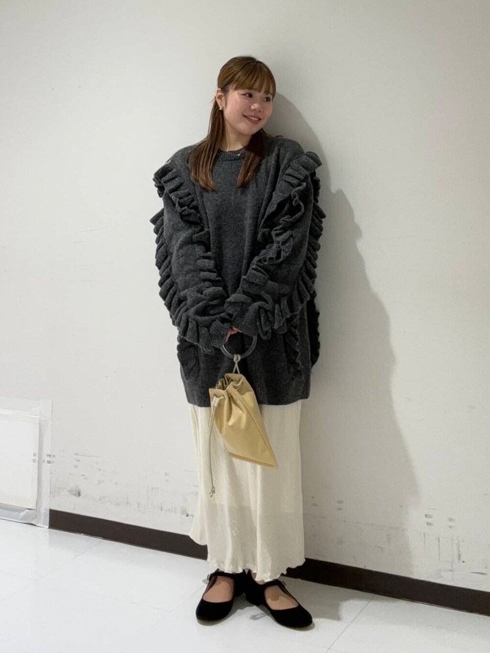 イエロー系のショルダーバッグ、ホワイト系のスカート、グレー系のニット/セーターを着用したレディースの冬コーディネートの4枚目の写真