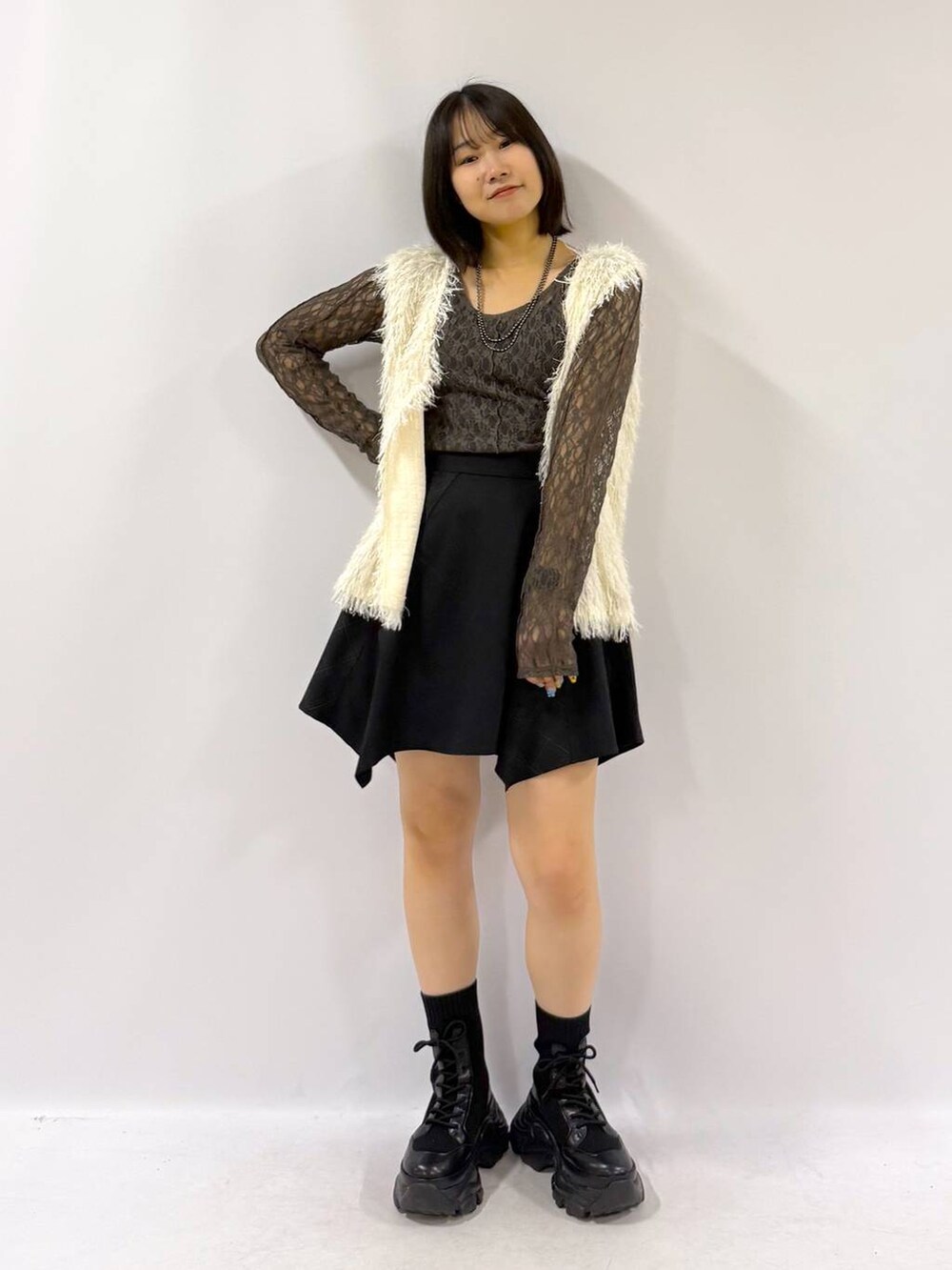 ブラック系のブーツ、ホワイト系のベスト、ブラック系のスカートを着用したレディースの秋コーディネートの7枚目の写真