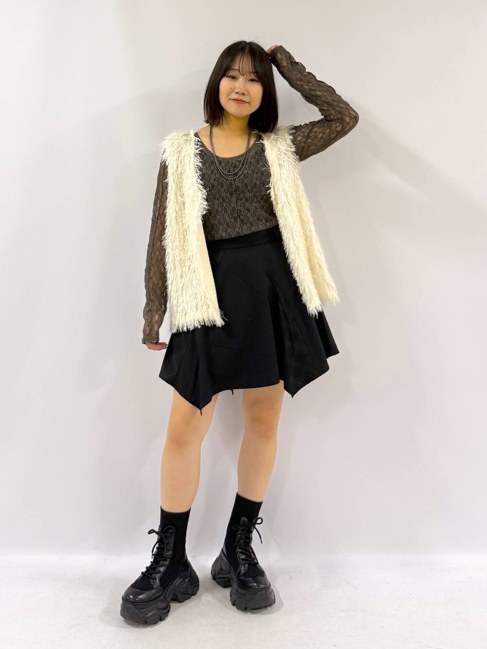 ブラック系のブーツ、ホワイト系のベスト、ブラック系のスカートを着用したレディースの秋コーディネートの4枚目の写真