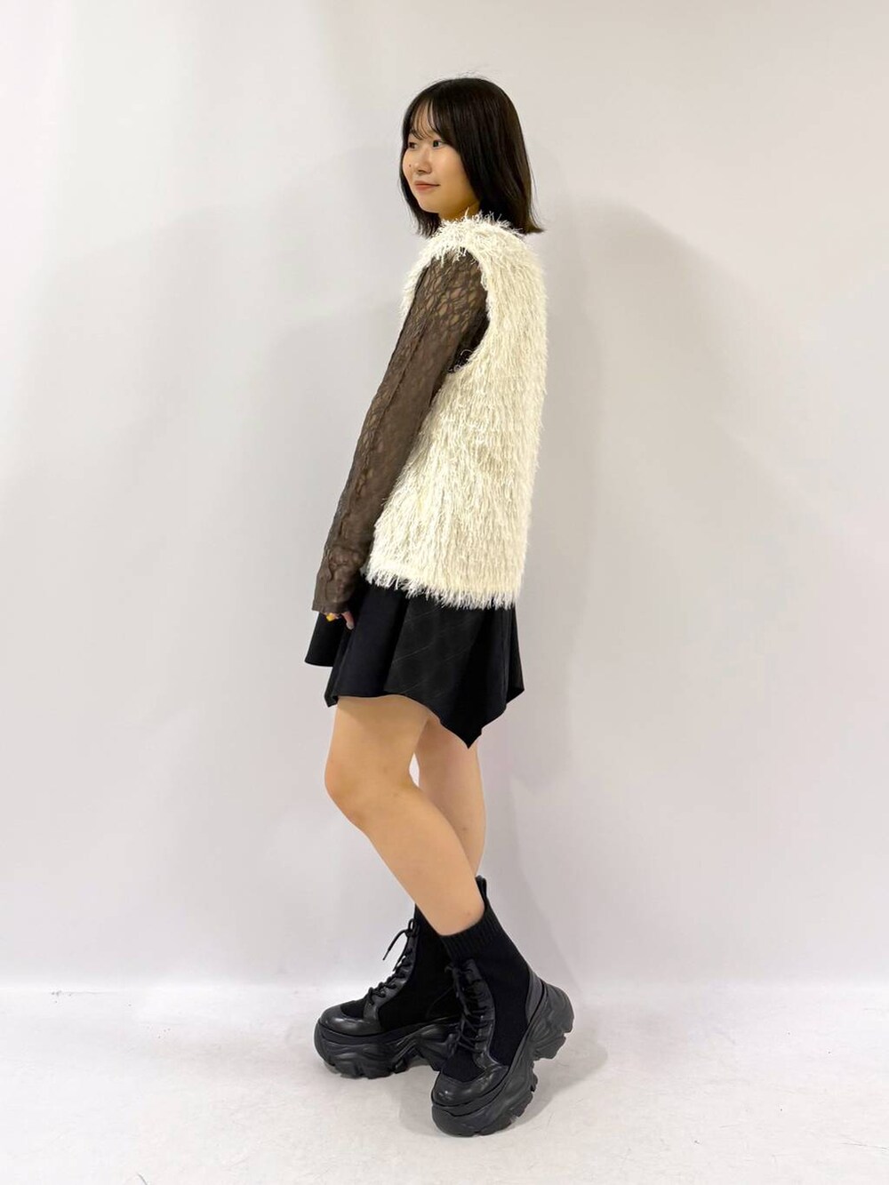 ブラック系のブーツ、ホワイト系のベスト、ブラック系のスカートを着用したレディースの秋コーディネートの5枚目の写真