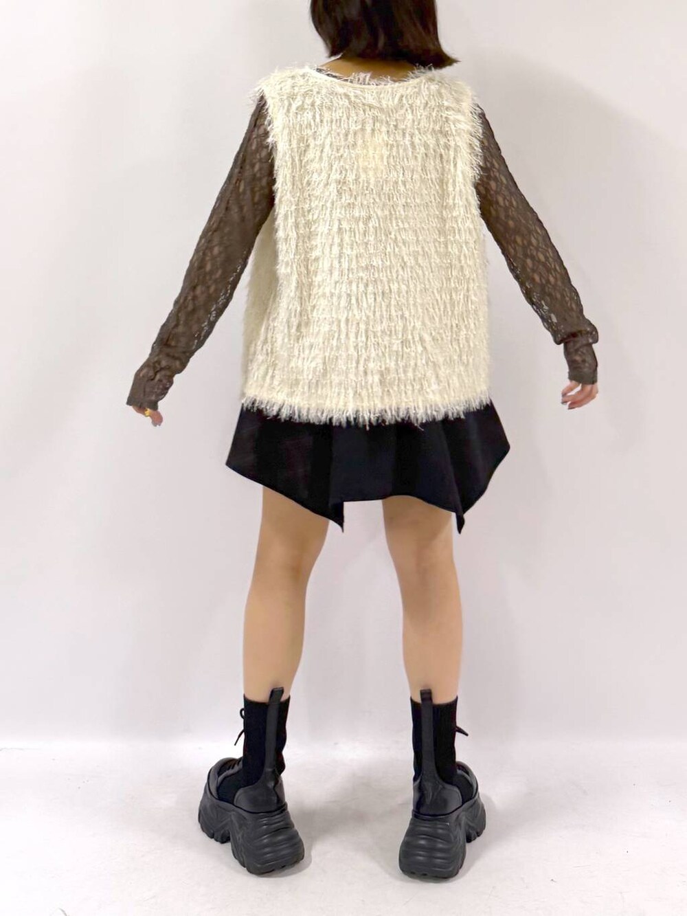 ブラック系のブーツ、ホワイト系のベスト、ブラック系のスカートを着用したレディースの秋コーディネートの2枚目の写真