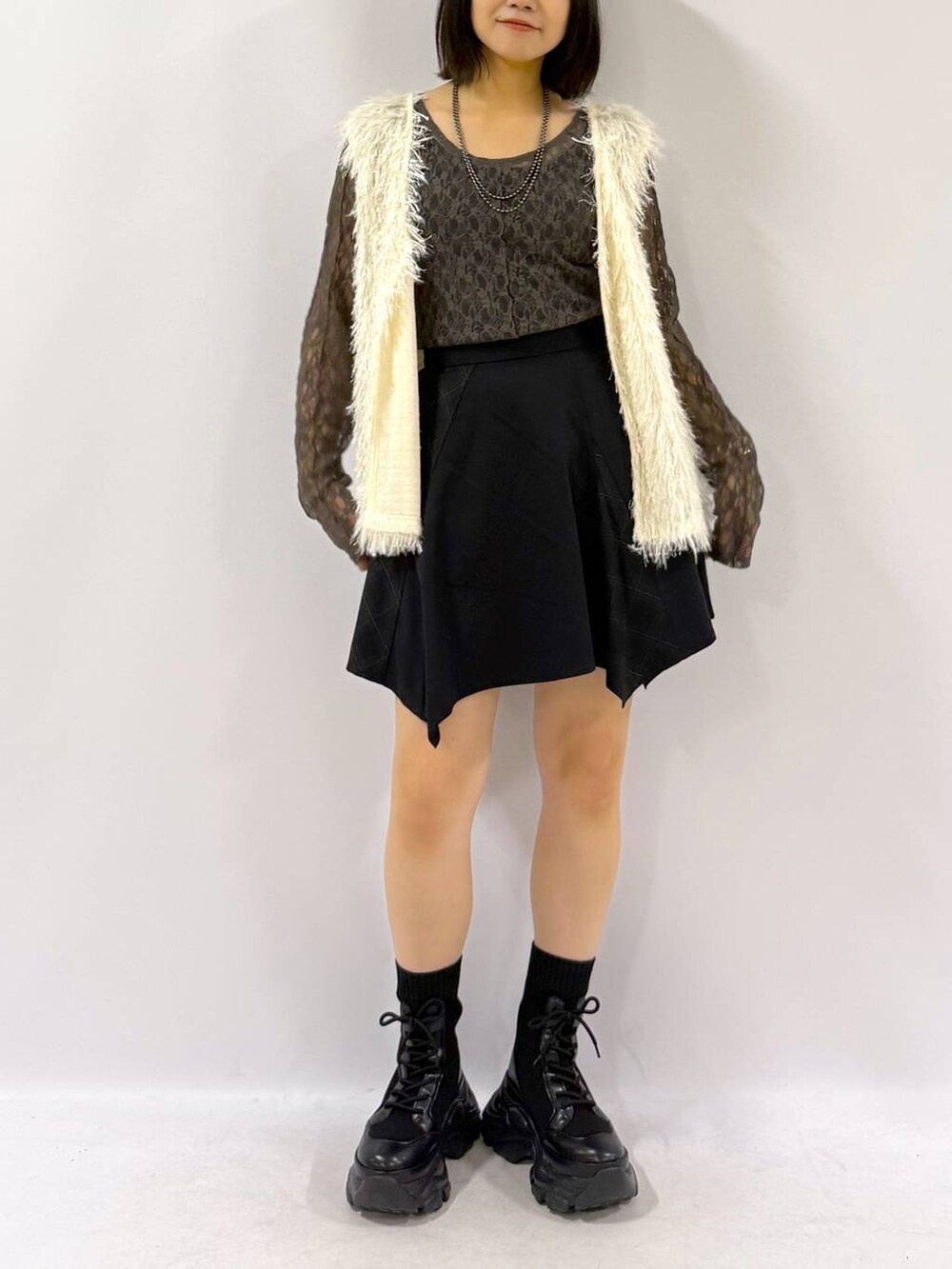 ブラック系のブーツ、ホワイト系のベスト、ブラック系のスカートを着用したレディースの秋コーディネートの3枚目の写真