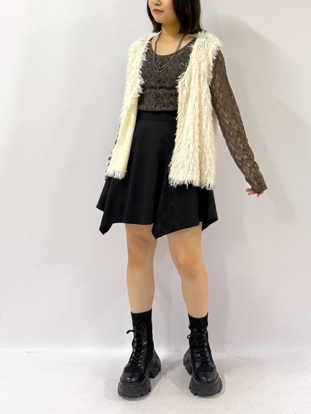 ブラック系のブーツ、ホワイト系のベスト、ブラック系のスカートを着用したレディースの秋コーディネートの6枚目の写真