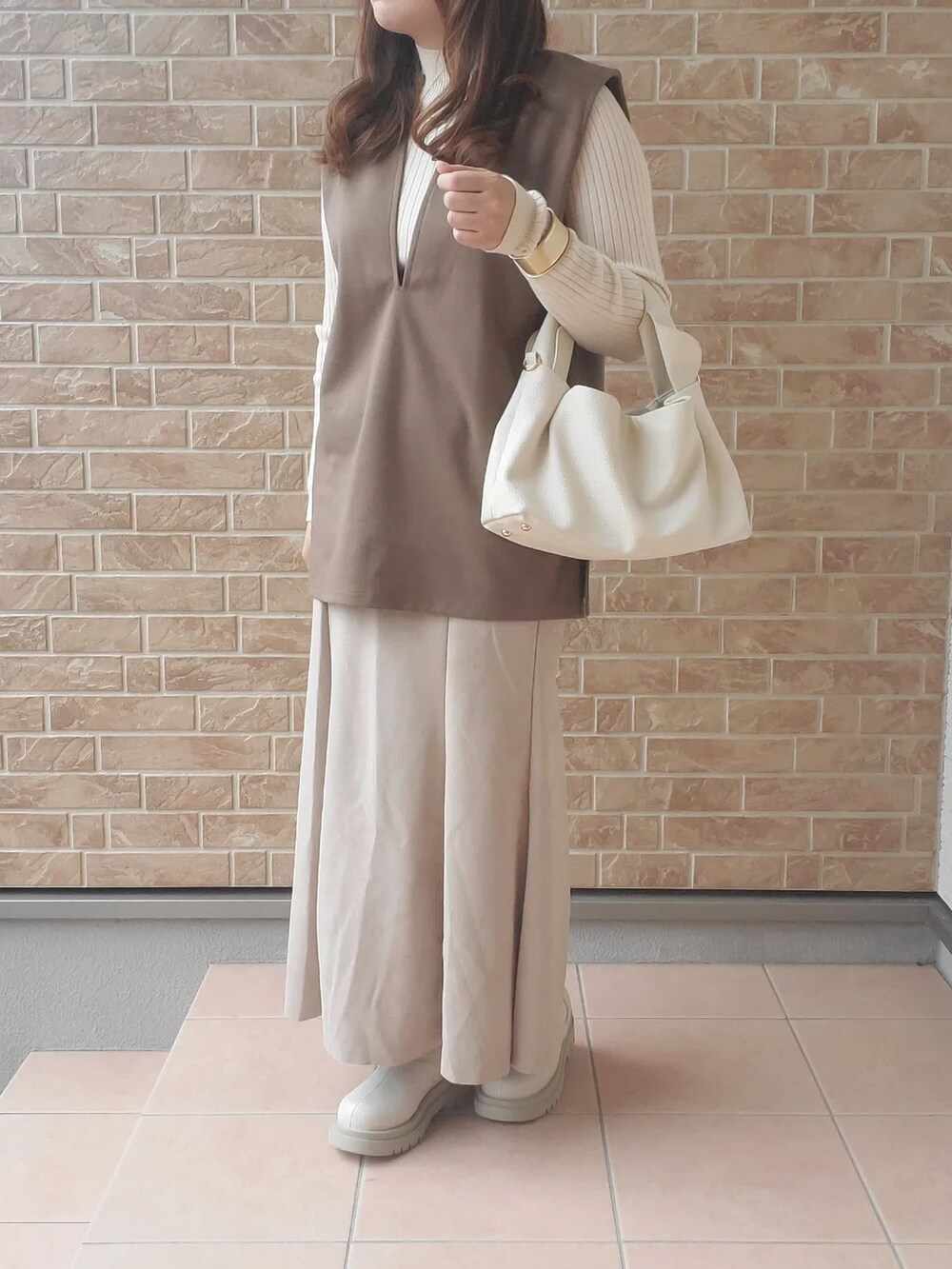 ホワイト系のブーツ、ブラウン系のベスト、ホワイト系のバッグを着用したレディースの秋コーディネートの2枚目の写真