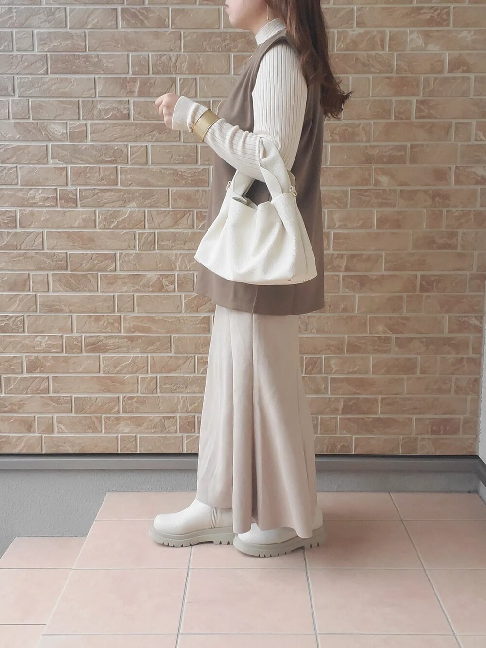 ホワイト系のブーツ、ブラウン系のベスト、ホワイト系のバッグを着用したレディースの秋コーディネートの3枚目の写真