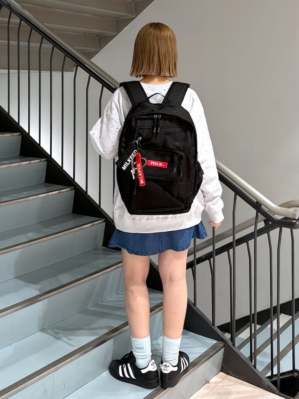 グレー系のスウェット、レッド系のバックパック/リュック、ブルー系のデニムスカートを着用したレディースの春コーディネートの2枚目の写真