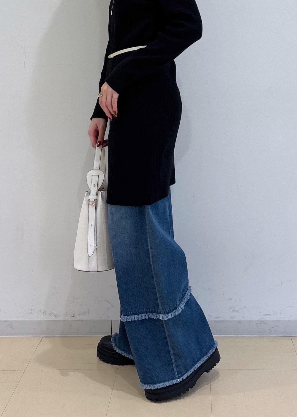 ブルー系のデニムパンツ、ブラック系のブーツ、ホワイト系のショルダーバッグを着用したレディースの秋コーディネートの5枚目の写真