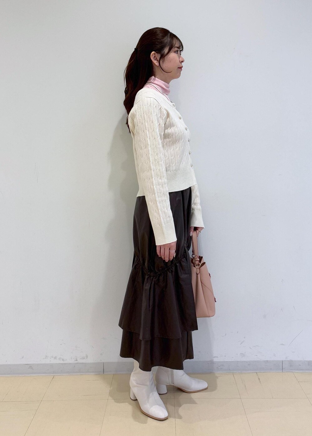 ピンク系のショルダーバッグ、ホワイト系のブーツ、ブラウン系のスカートを着用したレディースの冬コーディネートの3枚目の写真