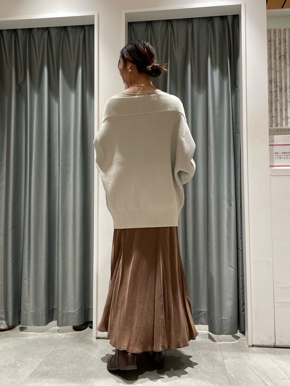 グレー系のニット/セーター、ブラウン系のスカート、ゴールド系のTシャツ/カットソーを着用したレディースの冬コーディネートの2枚目の写真