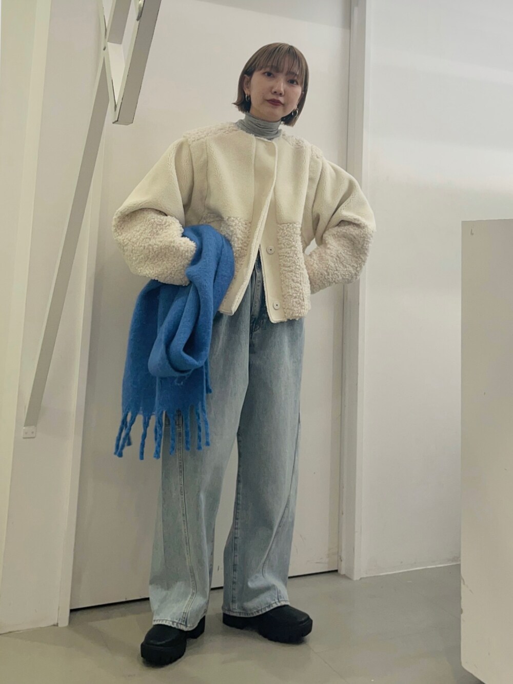 ホワイト系のブルゾン、ブルー系のデニムパンツ、ブルー系のマフラーを着用したレディースの冬コーディネートの4枚目の写真