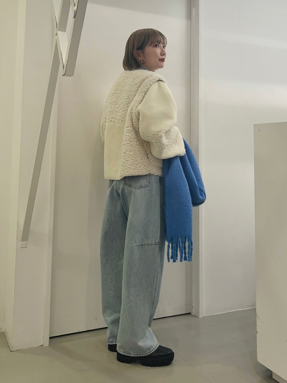 ホワイト系のブルゾン、ブルー系のデニムパンツ、ブルー系のマフラーを着用したレディースの冬コーディネートの3枚目の写真