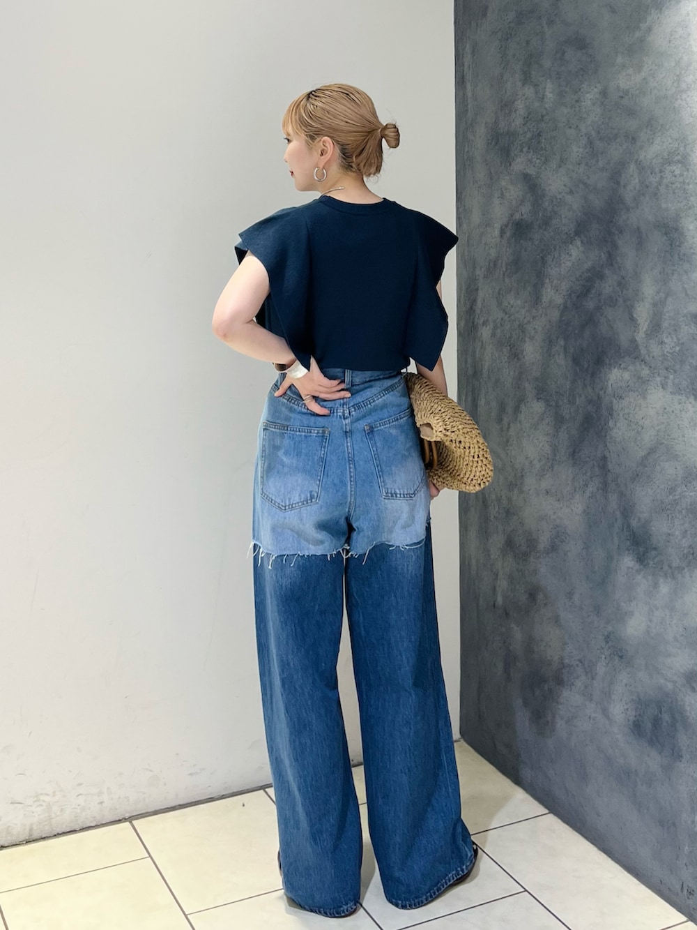 ブルー系のデニムパンツ、ブルー系のニット/セーター、ベージュ系のトートバッグを着用したレディースの夏コーディネートの3枚目の写真