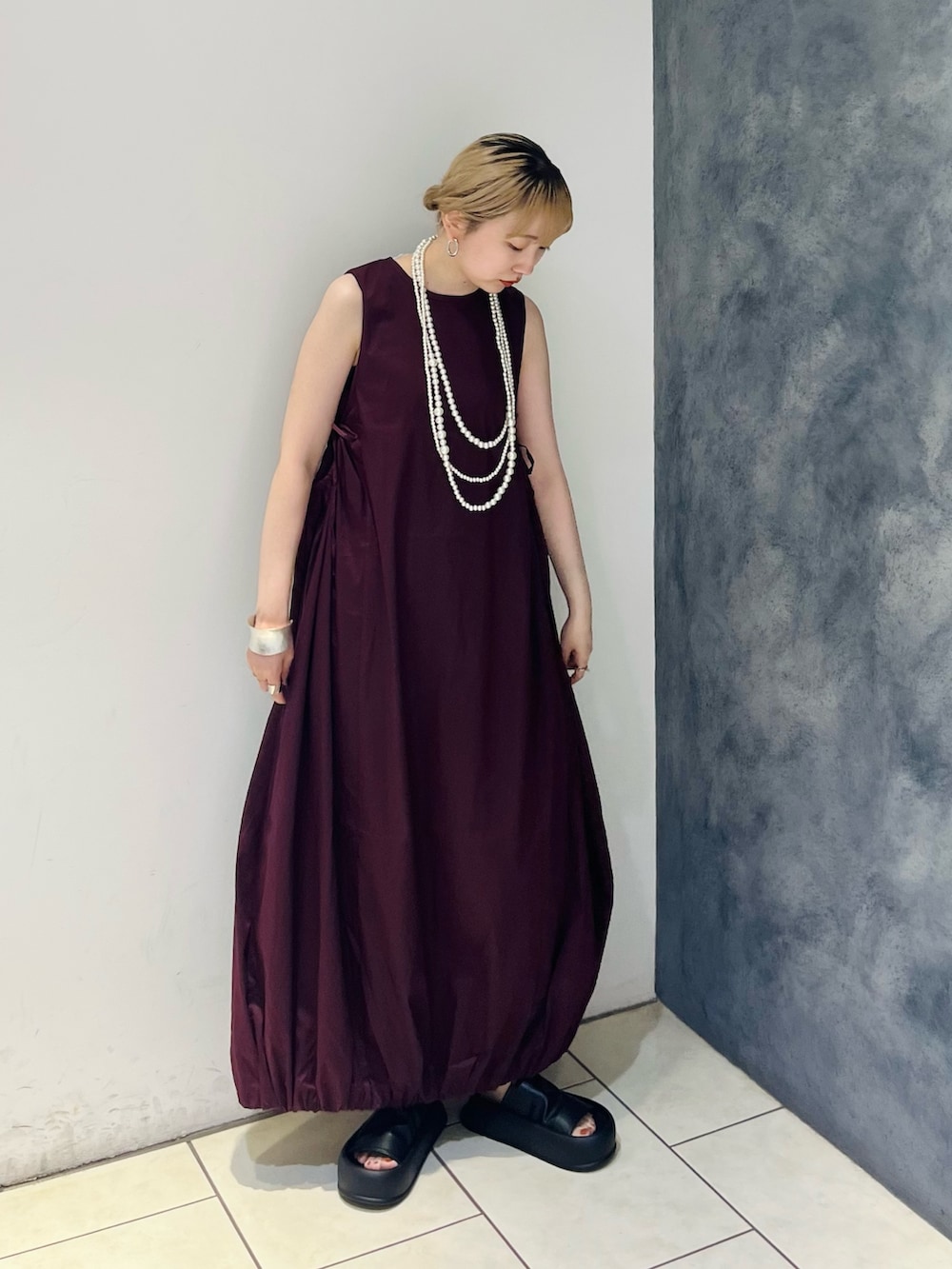 レッド系のワンピース、ブラック系のサンダル、ホワイト系のネックレスを着用したレディースの夏コーディネートの2枚目の写真