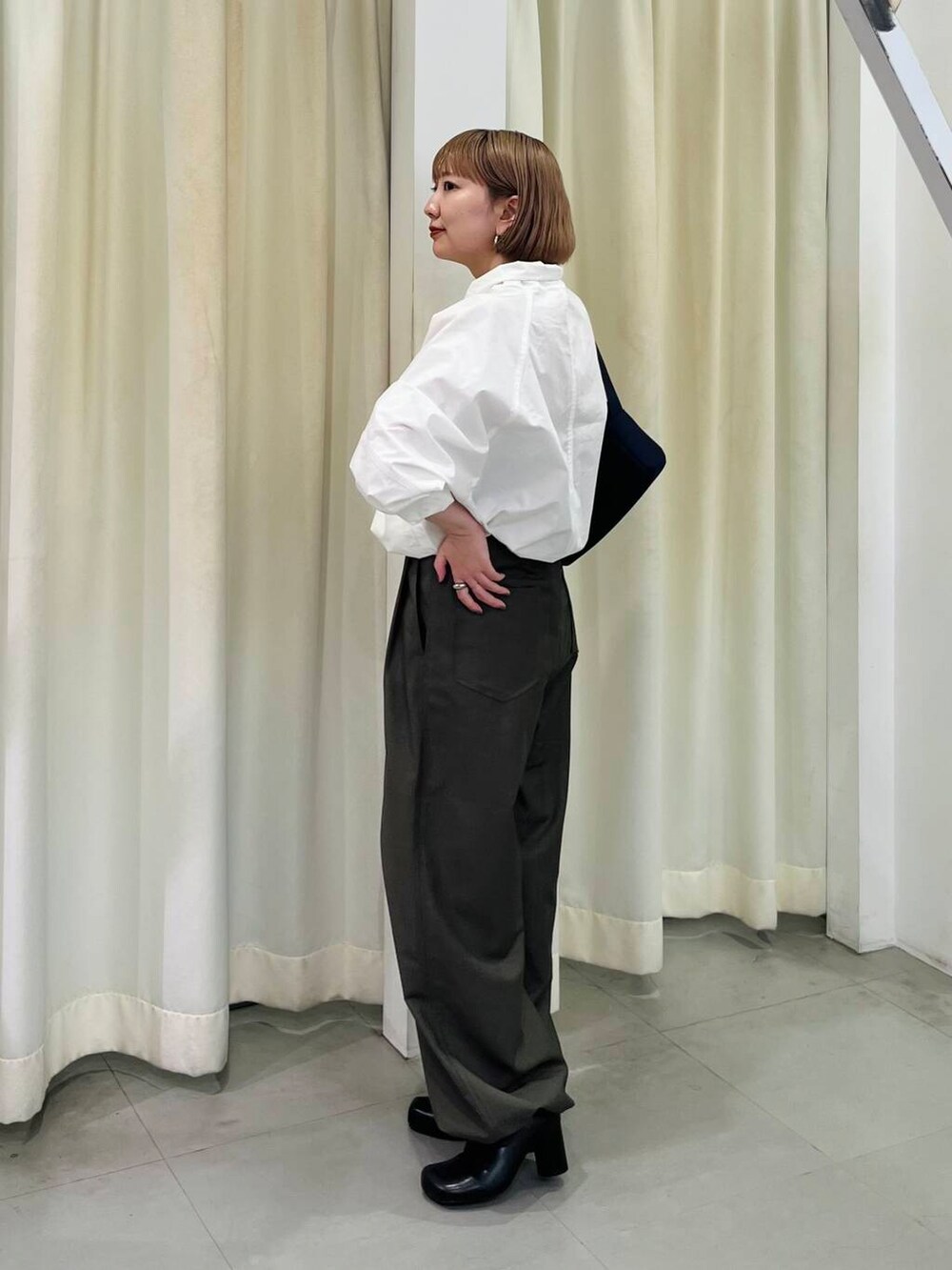 ブラック系のブーツ、ブルー系のショルダーバッグ、グリーン系のスラックスを着用したレディースの秋コーディネートの3枚目の写真