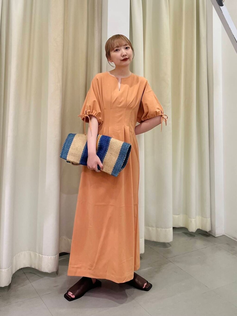 オレンジ系のワンピース、ブラウン系のサンダル、その他のトートバッグを着用したレディースの夏コーディネートの2枚目の写真