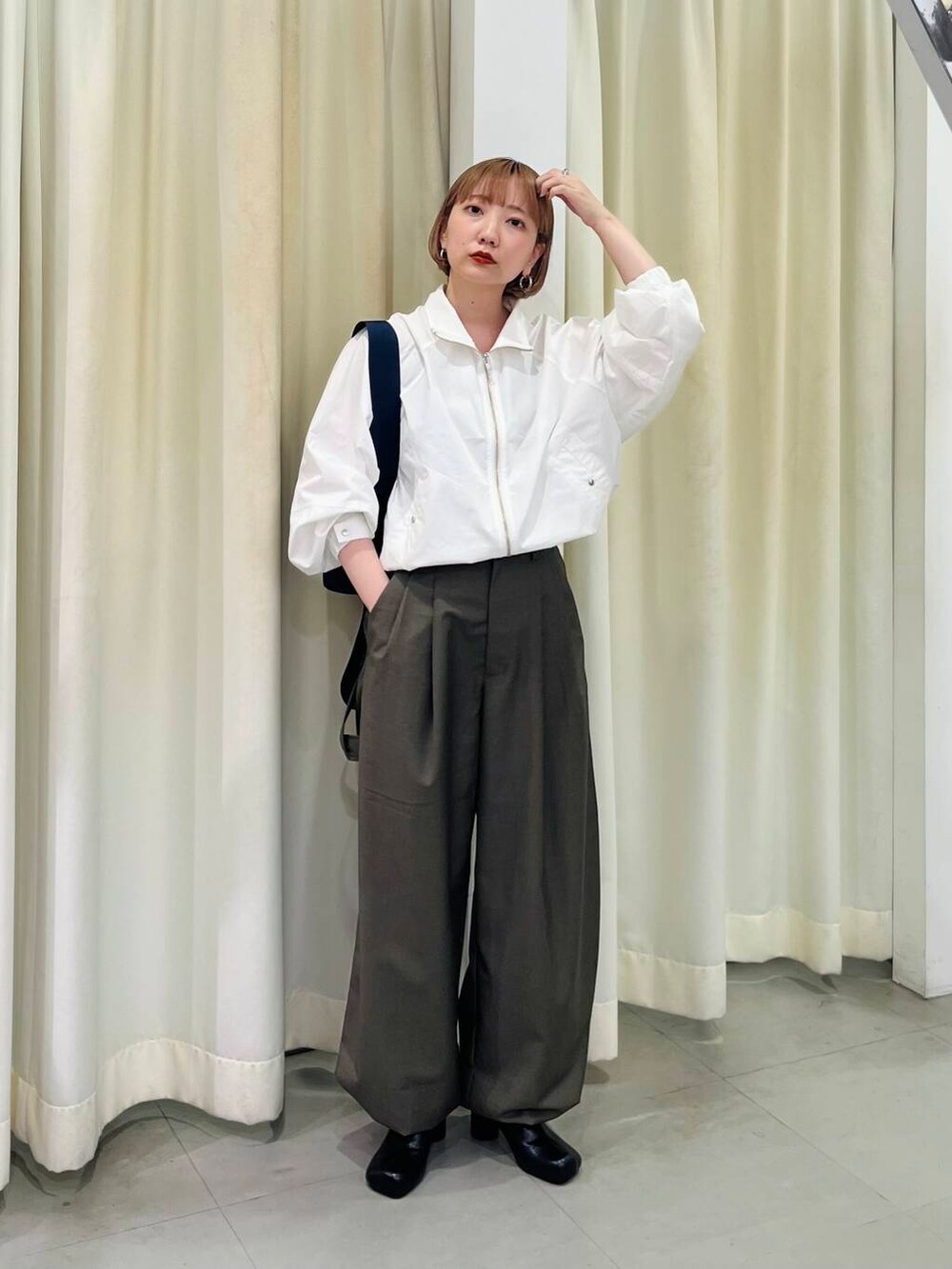 ブラック系のブーツ、ブルー系のショルダーバッグ、グリーン系のスラックスを着用したレディースの秋コーディネートの2枚目の写真