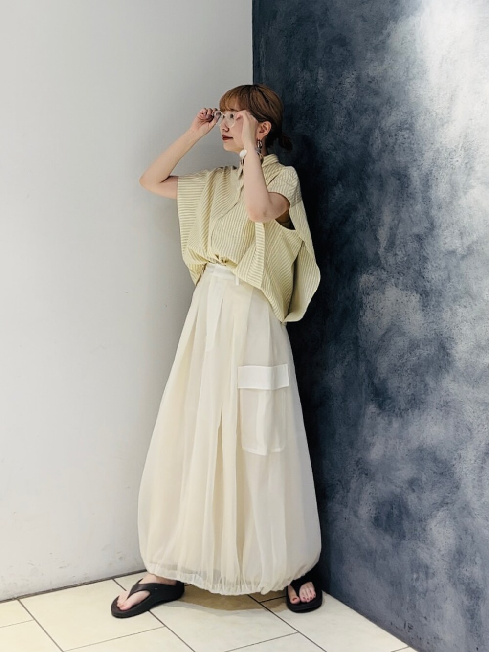 イエロー系のシャツ/ブラウス、ホワイト系のスカート、ブラウン系のサンダルを着用したレディースの春コーディネートの2枚目の写真