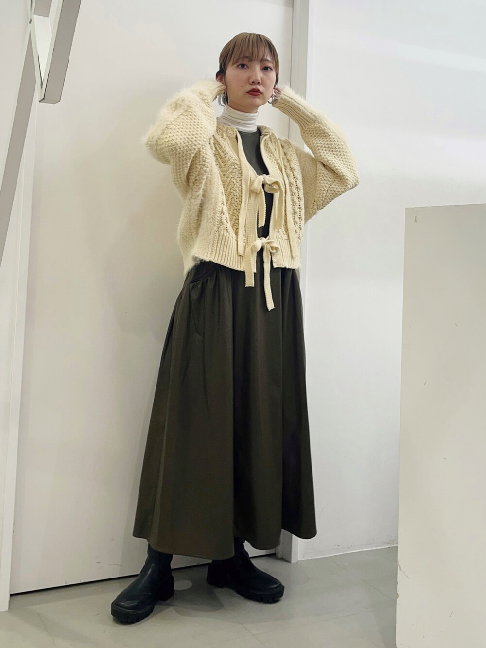 ホワイト系のニット/セーター、ブラウン系のワンピース、ブラック系のブーツを着用したレディースの冬コーディネートの2枚目の写真