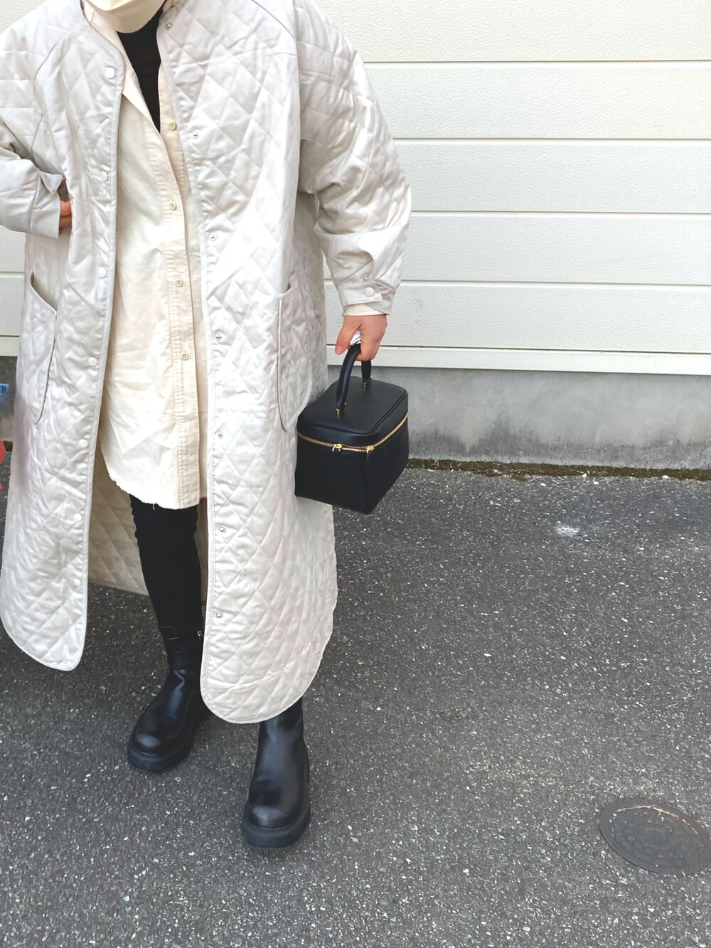 ホワイト系のノーカラーコート、ブラック系のブーツ、ブラック系のハンドバッグを着用したレディースの冬コーディネートの2枚目の写真