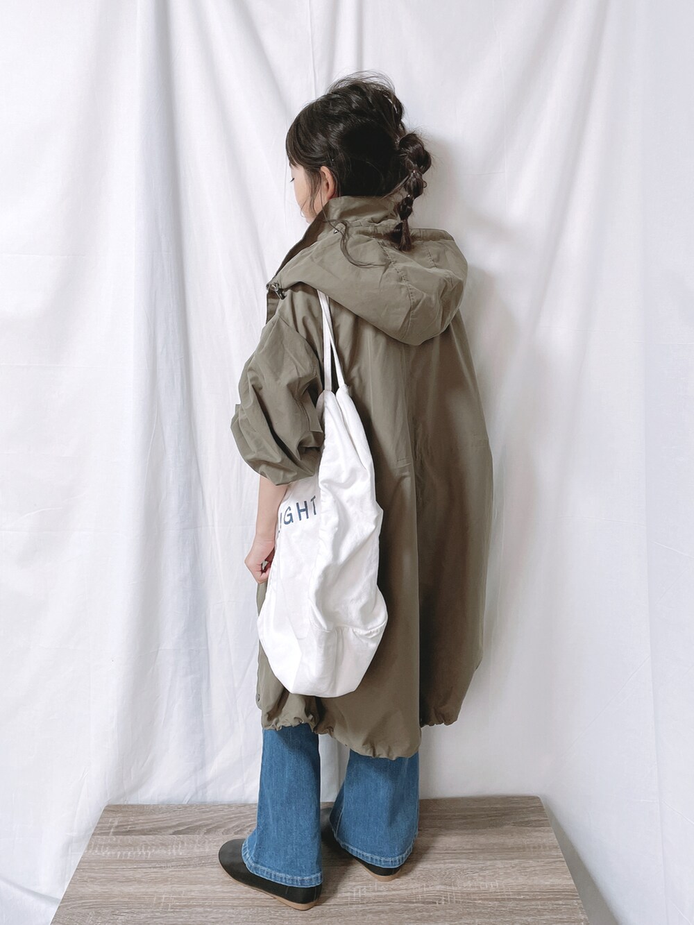 グリーン系のモッズコート、ブルー系のデニムパンツ、ホワイト系のトートバッグを着用したキッズの秋コーディネートの2枚目の写真