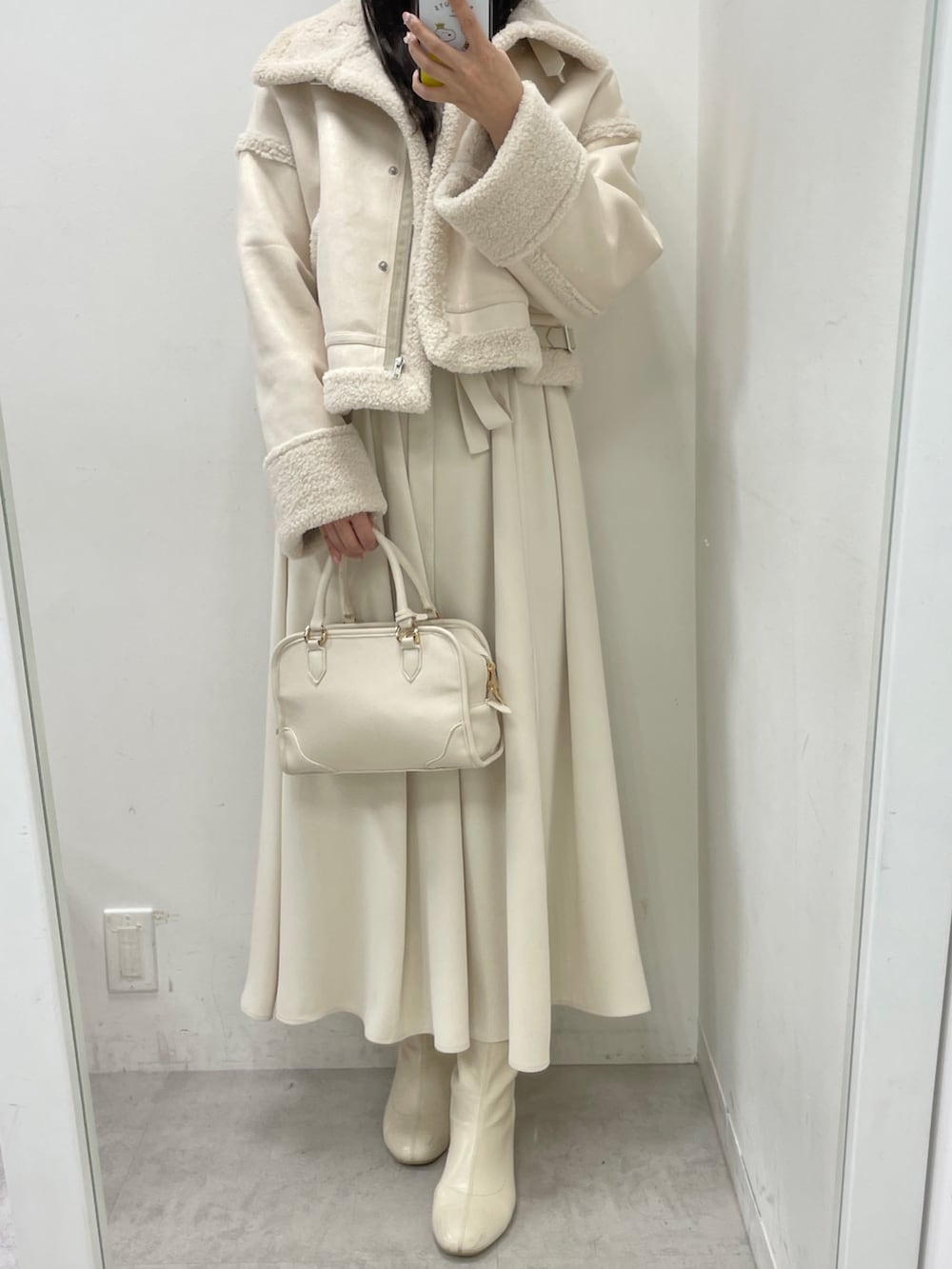 ホワイト系のムートンコート、ホワイト系のハンドバッグ、ベージュ系のワンピースを着用したレディースの冬コーディネートの2枚目の写真