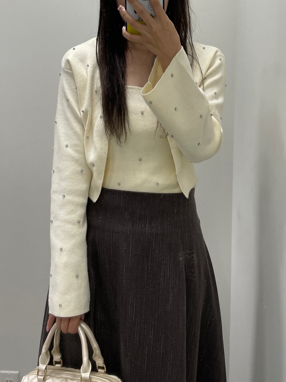 ホワイト系のカーディガン/ボレロ、ホワイト系のキャミソール、ブラウン系のスカートを着用したレディースの秋コーディネートの3枚目の写真