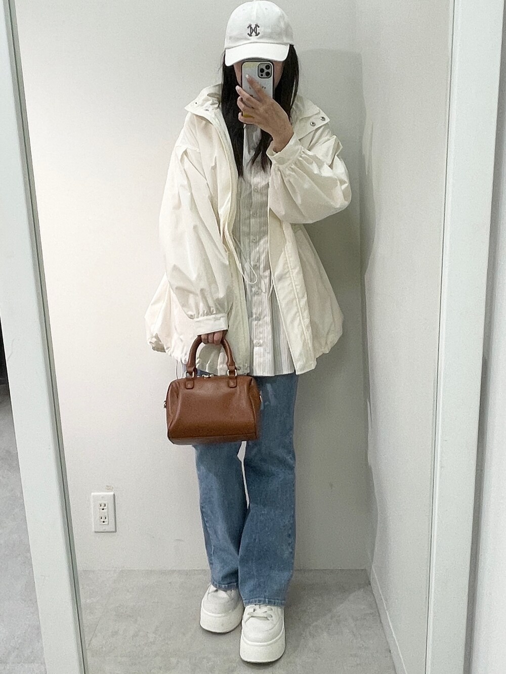 ホワイト系のマウンテンパーカー、ブラウン系のボストンバッグ、ブルー系のデニムパンツを着用したレディースの春コーディネートの2枚目の写真