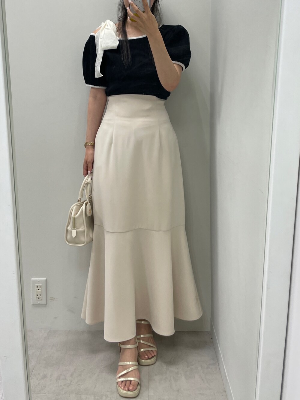 ブラック系のニット/セーター、ベージュ系のスカート、ホワイト系のハンドバッグを着用したレディースの夏コーディネートの2枚目の写真