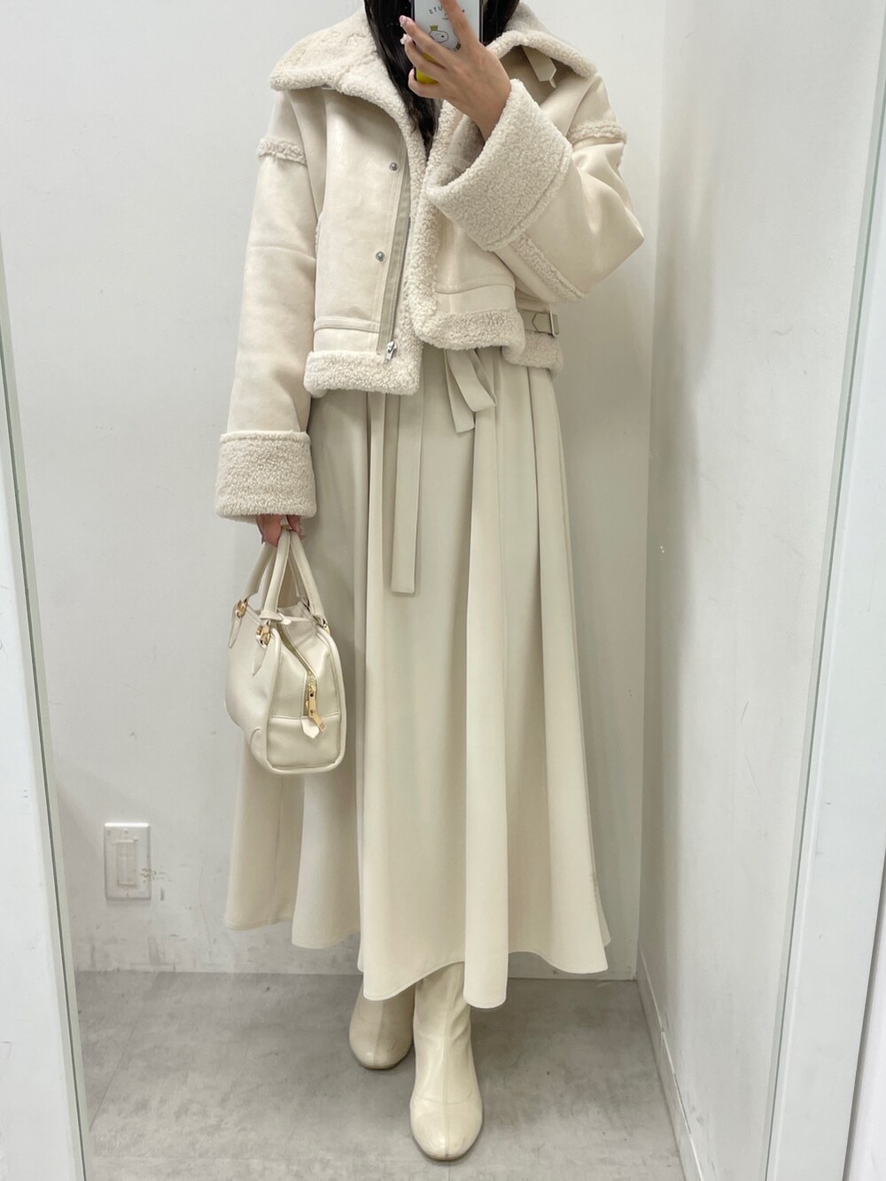 ホワイト系のムートンコート、ホワイト系のハンドバッグ、ベージュ系のワンピースを着用したレディースの冬コーディネートの3枚目の写真