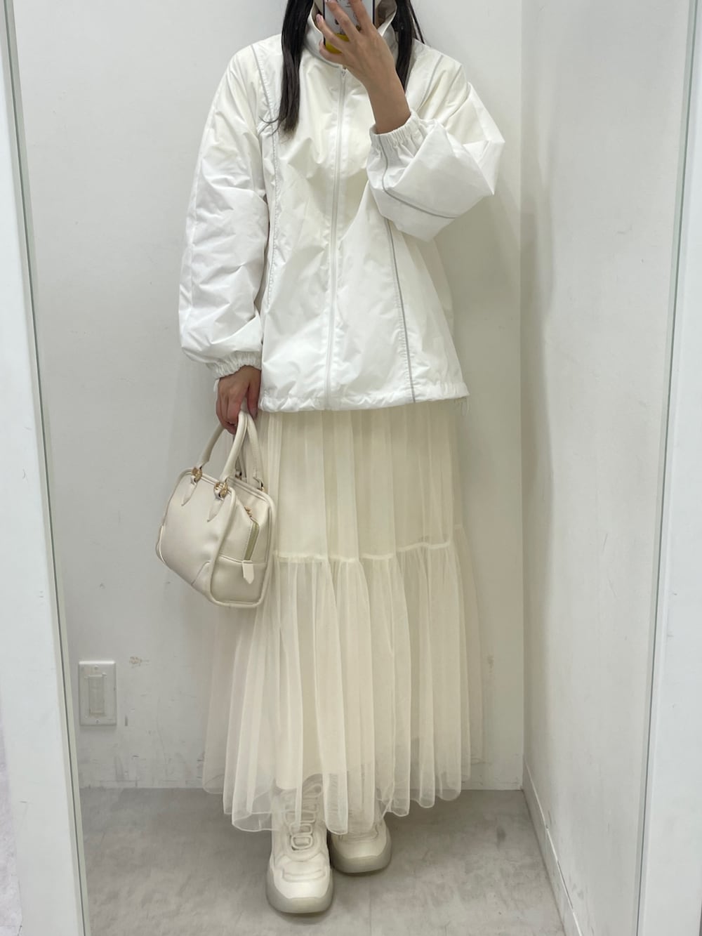 ホワイト系のナイロンジャケット、ホワイト系のスカート、ホワイト系のスニーカーを着用したレディースの冬コーディネートの2枚目の写真