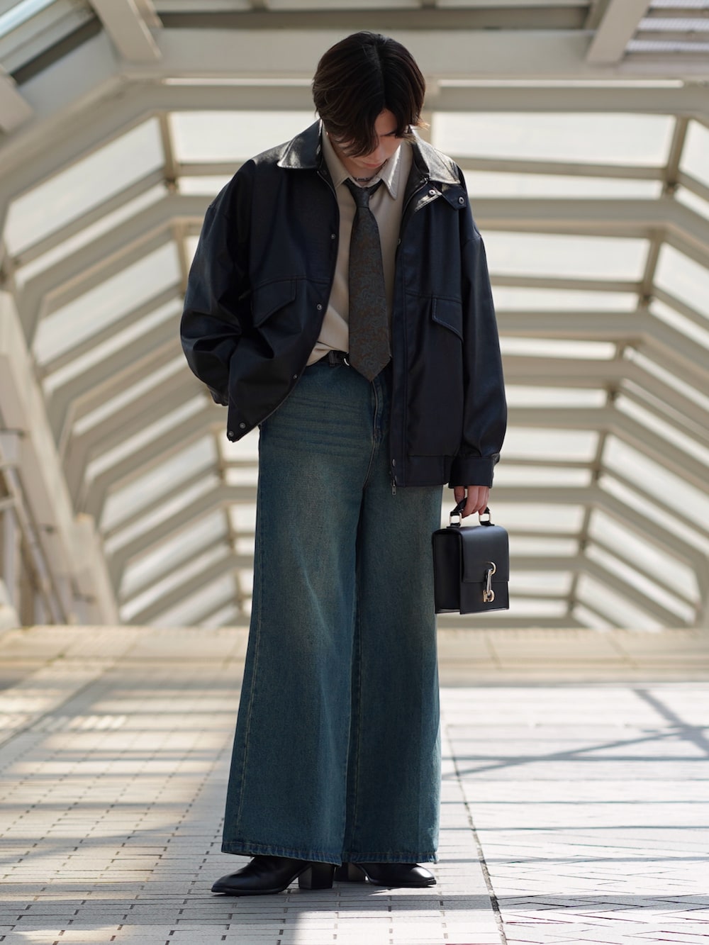 ブラック系のブルゾン、ベージュ系のシャツ/ブラウス、ブルー系のデニムパンツを着用したメンズの春コーディネートの2枚目の写真