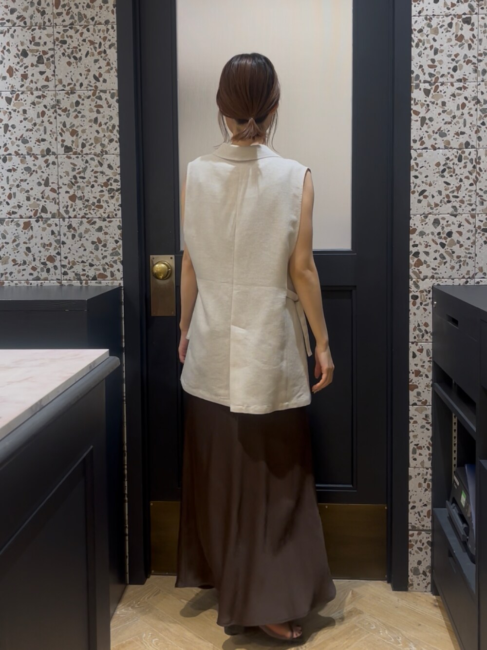 ブラウン系のスカート、ブラウン系のサンダル、ベージュ系のベストを着用したレディースの夏コーディネートの2枚目の写真