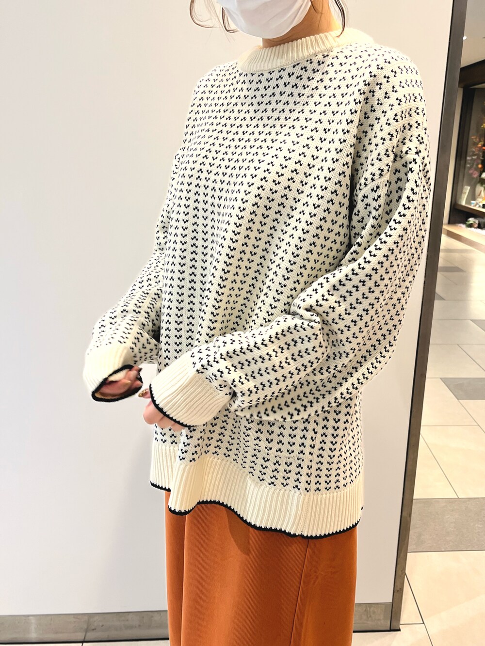 オレンジ系のスカート、ホワイト系のニット/セーター、ブラック系のブーツを着用したレディースの秋コーディネートの2枚目の写真