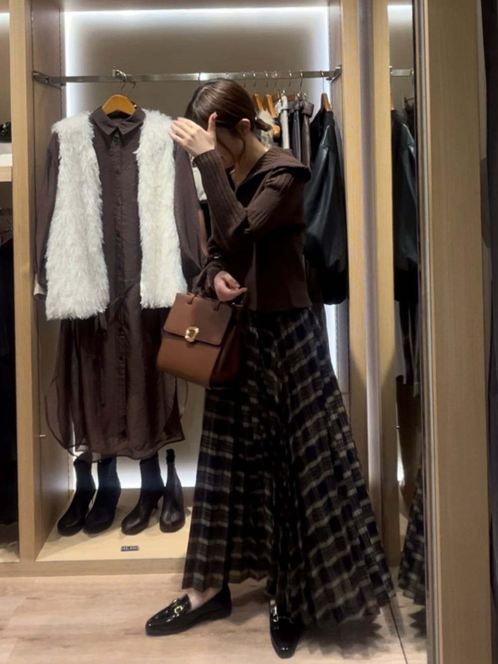 オレンジ系のニット/セーター、ブラウン系のハンドバッグ、ブルー系のスカートを着用したレディースの秋コーディネートの2枚目の写真