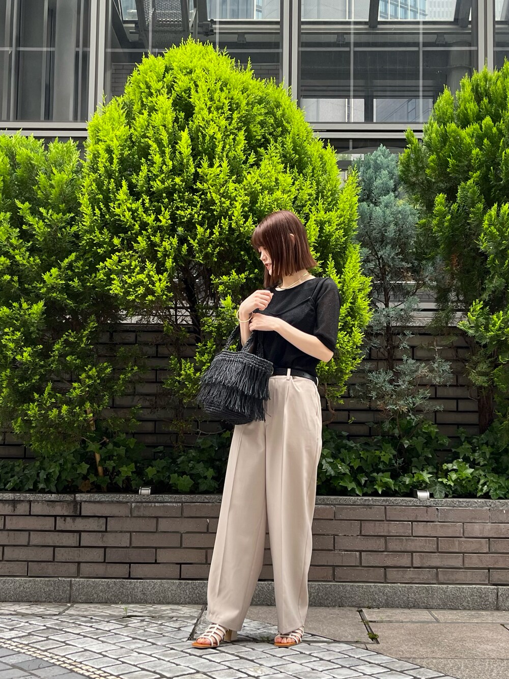 ブラック系のTシャツ/カットソー、ブラック系のハンドバッグ、ベージュ系のスラックスを着用したレディースの春コーディネートの2枚目の写真