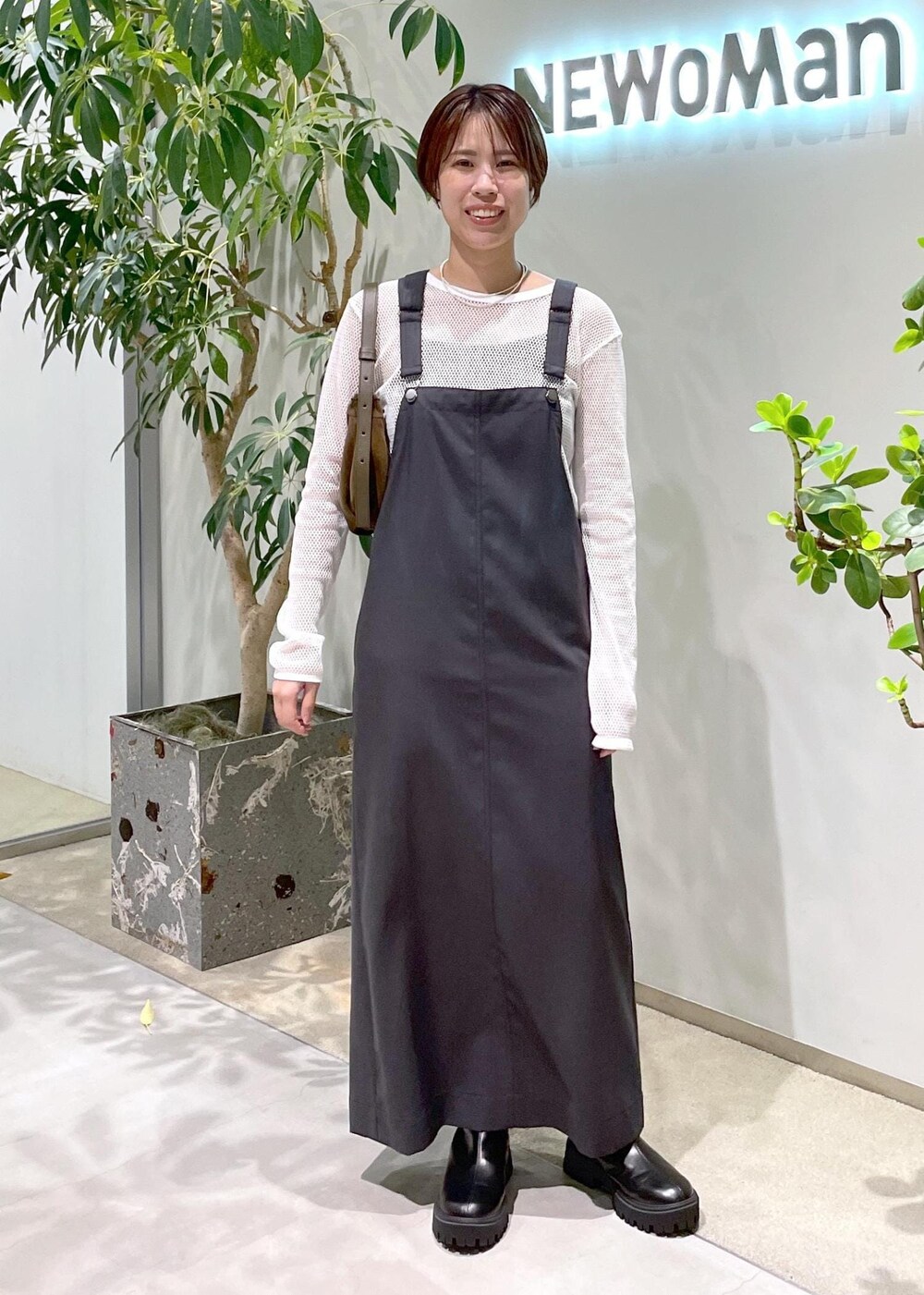 ブラック系のブーツ、グレー系のジャンパースカート、ブラウン系のショルダーバッグを着用したレディースの秋コーディネートの2枚目の写真