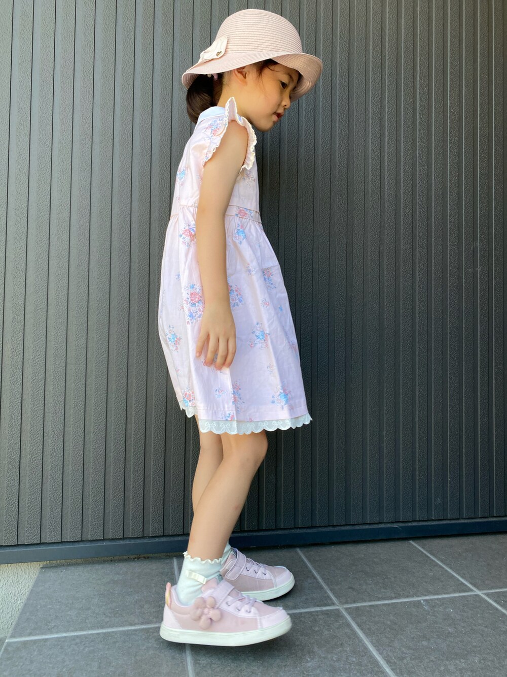 オレンジ系のジャンパースカート、ピンク系のスニーカー、ピンク系のハットを着用したキッズの夏コーディネートの3枚目の写真