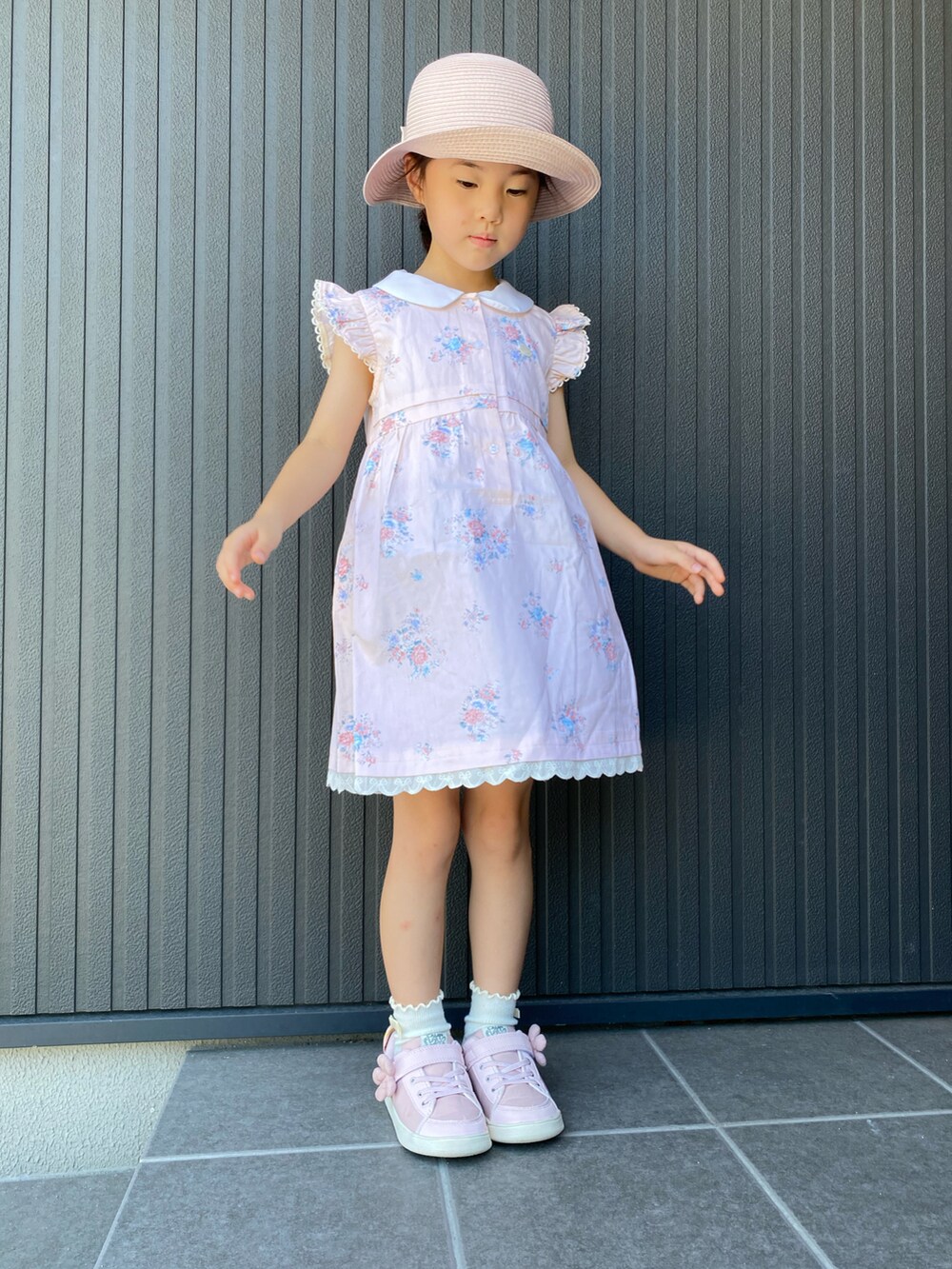 オレンジ系のジャンパースカート、ピンク系のスニーカー、ピンク系のハットを着用したキッズの夏コーディネートの2枚目の写真