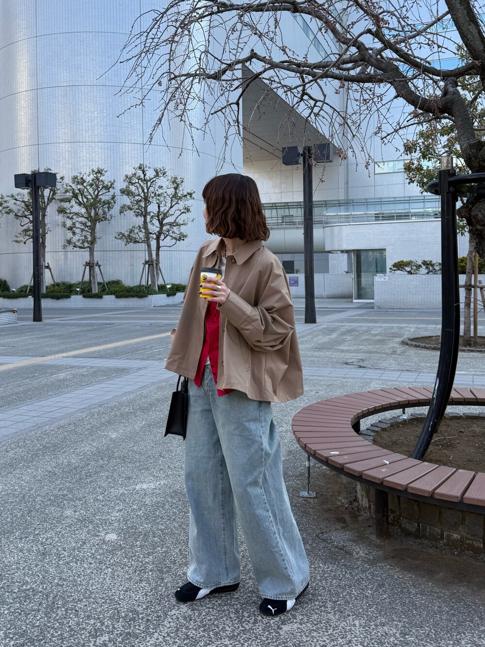 ベージュ系のステンカラーコート、レッド系のTシャツ/カットソー、ブルー系のデニムパンツを着用したレディースの春コーディネートの3枚目の写真