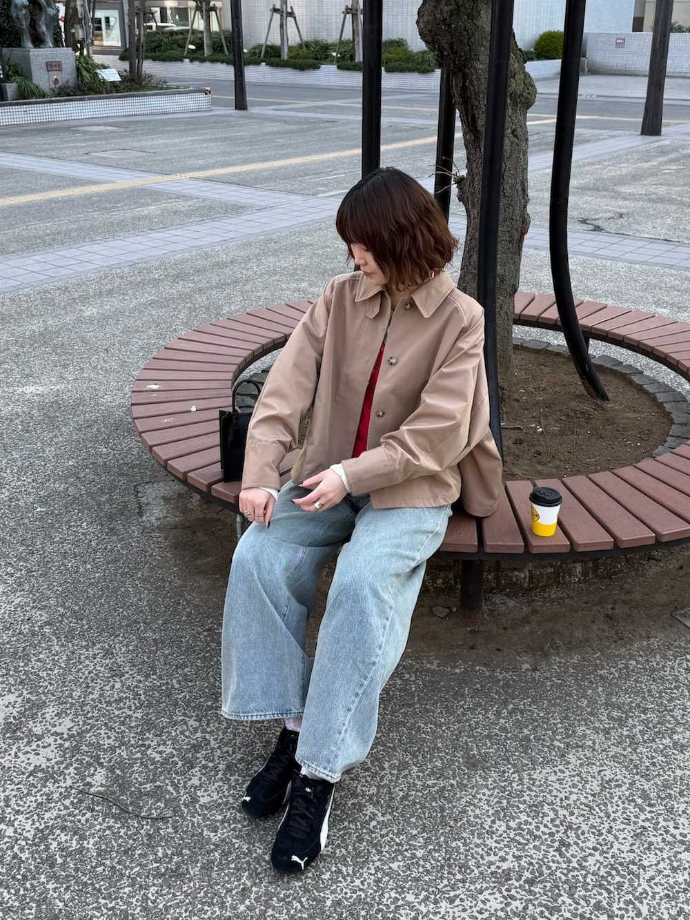 ベージュ系のステンカラーコート、レッド系のTシャツ/カットソー、ブルー系のデニムパンツを着用したレディースの春コーディネートの2枚目の写真