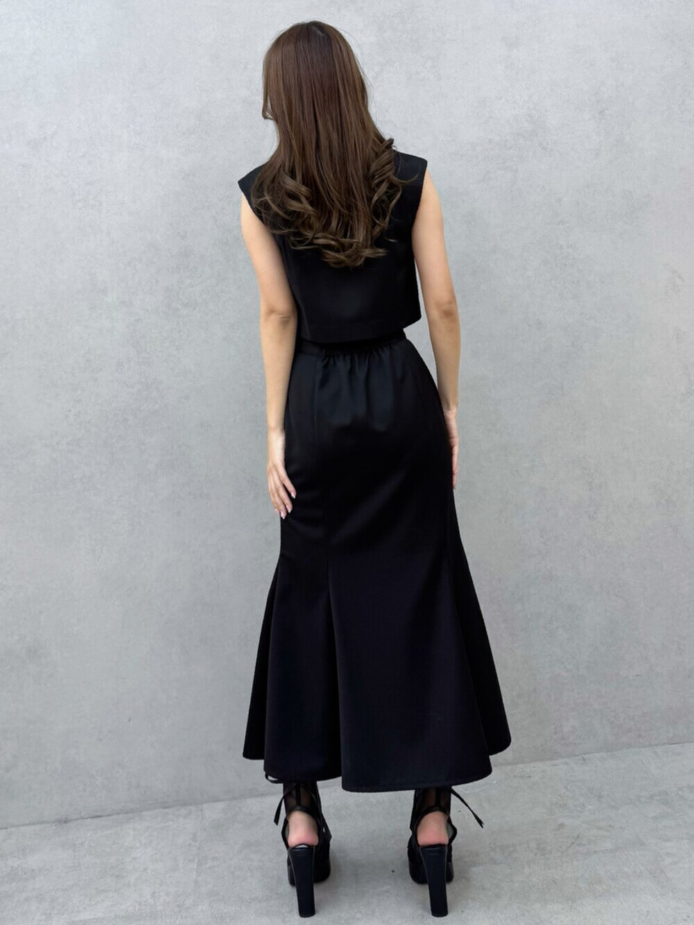 ブラック系のサンダル、ブラック系のベスト、ブラック系のスカートを着用したレディースの春コーディネートの4枚目の写真