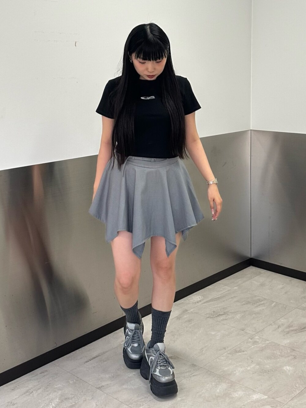 シルバー系のスニーカー、グレー系のスカート、ブラック系のTシャツ/カットソーを着用したレディースの春コーディネートの2枚目の写真
