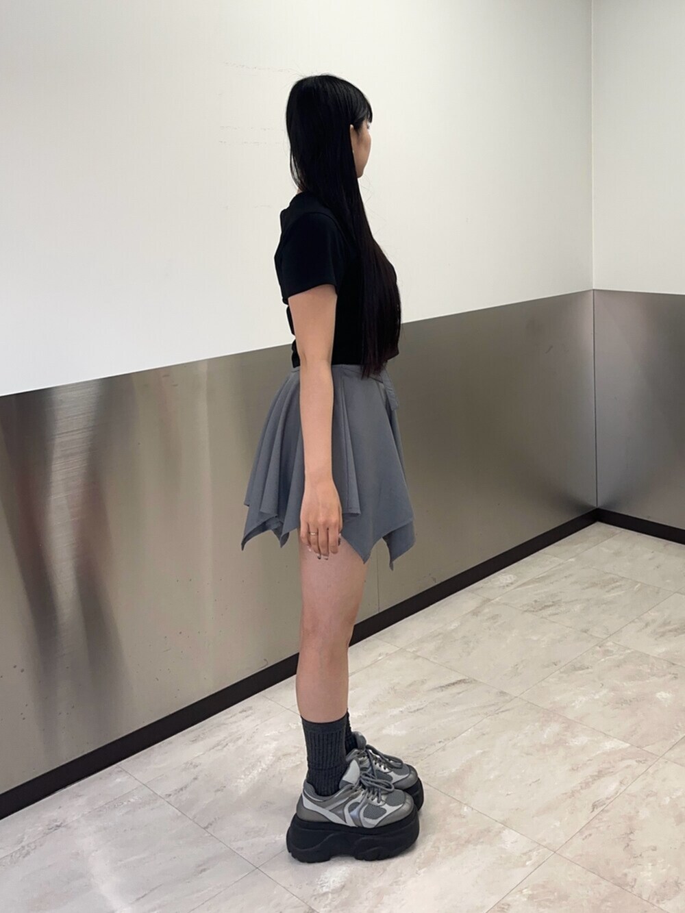 シルバー系のスニーカー、グレー系のスカート、ブラック系のTシャツ/カットソーを着用したレディースの春コーディネートの3枚目の写真
