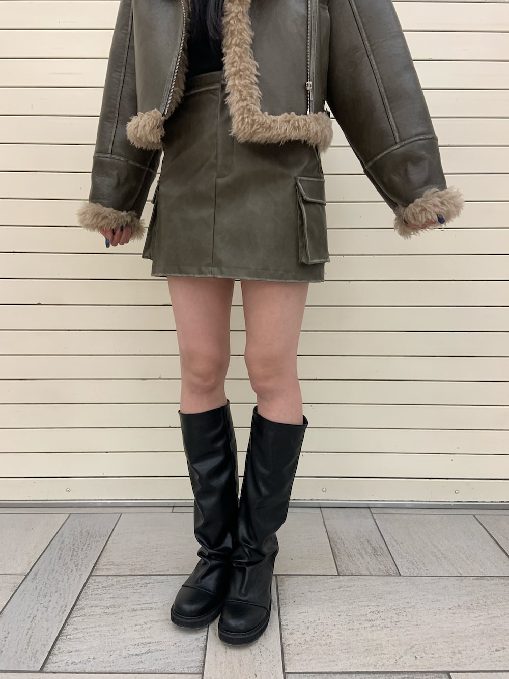 グリーン系のムートンコート、ブラック系のニット/セーター、グリーン系のスカートを着用したレディースの冬コーディネートの6枚目の写真