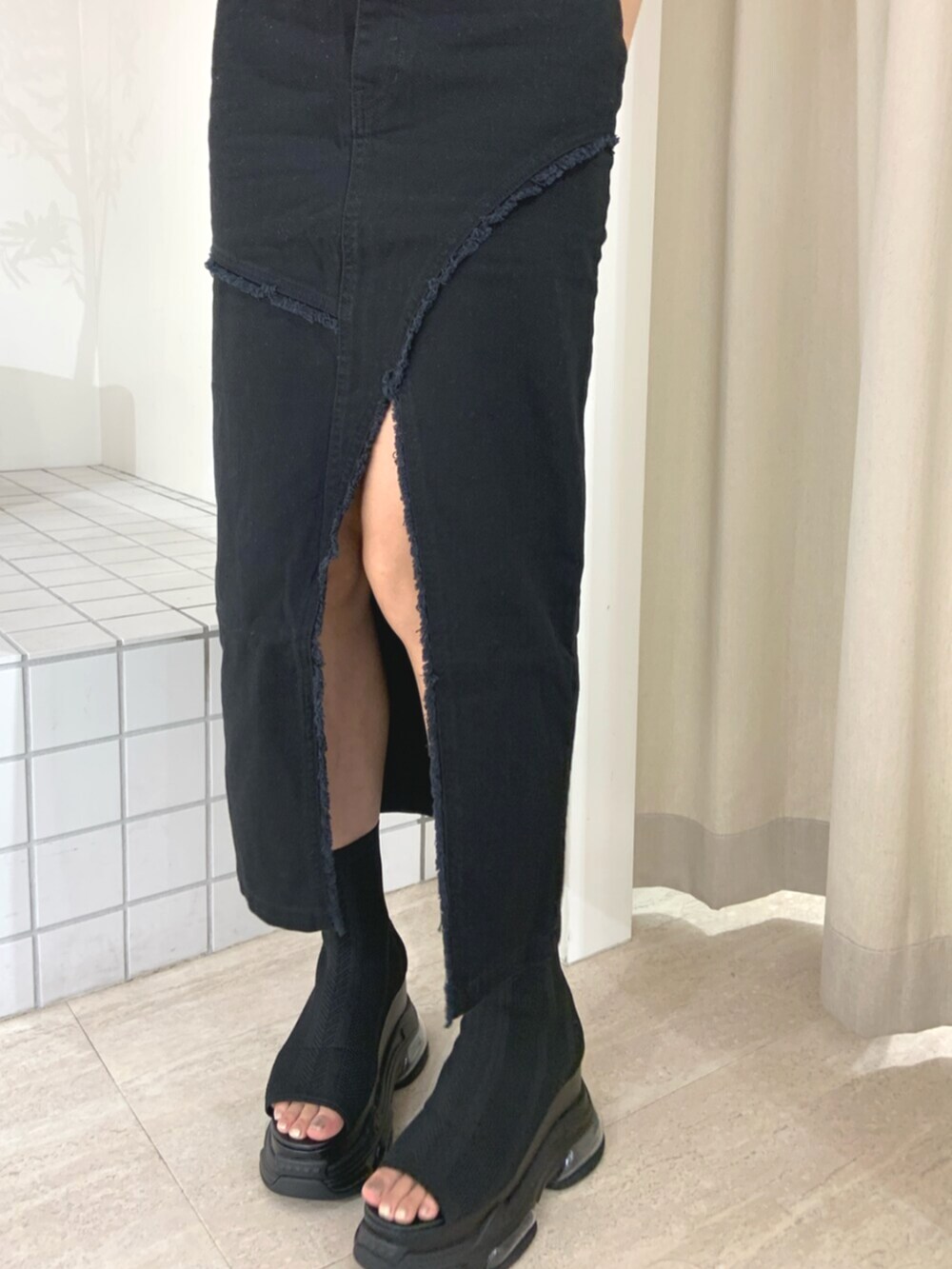 グレー系のベスト、ブラック系のサンダル、ブラック系のデニムスカートを着用したレディースの夏コーディネートの5枚目の写真