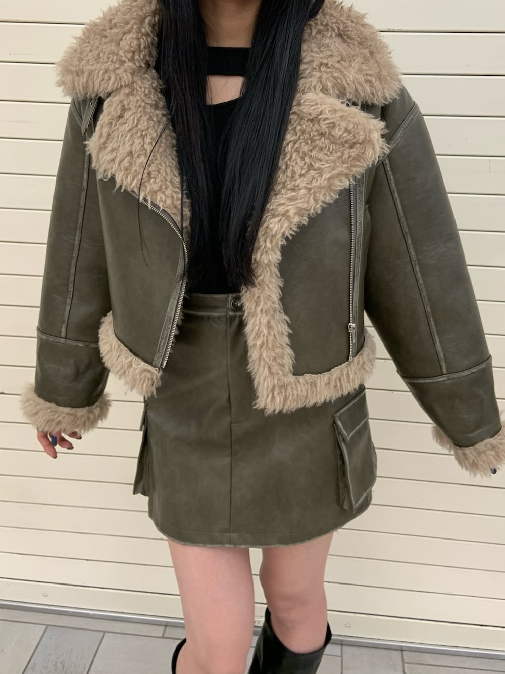 グリーン系のムートンコート、ブラック系のニット/セーター、グリーン系のスカートを着用したレディースの冬コーディネートの5枚目の写真