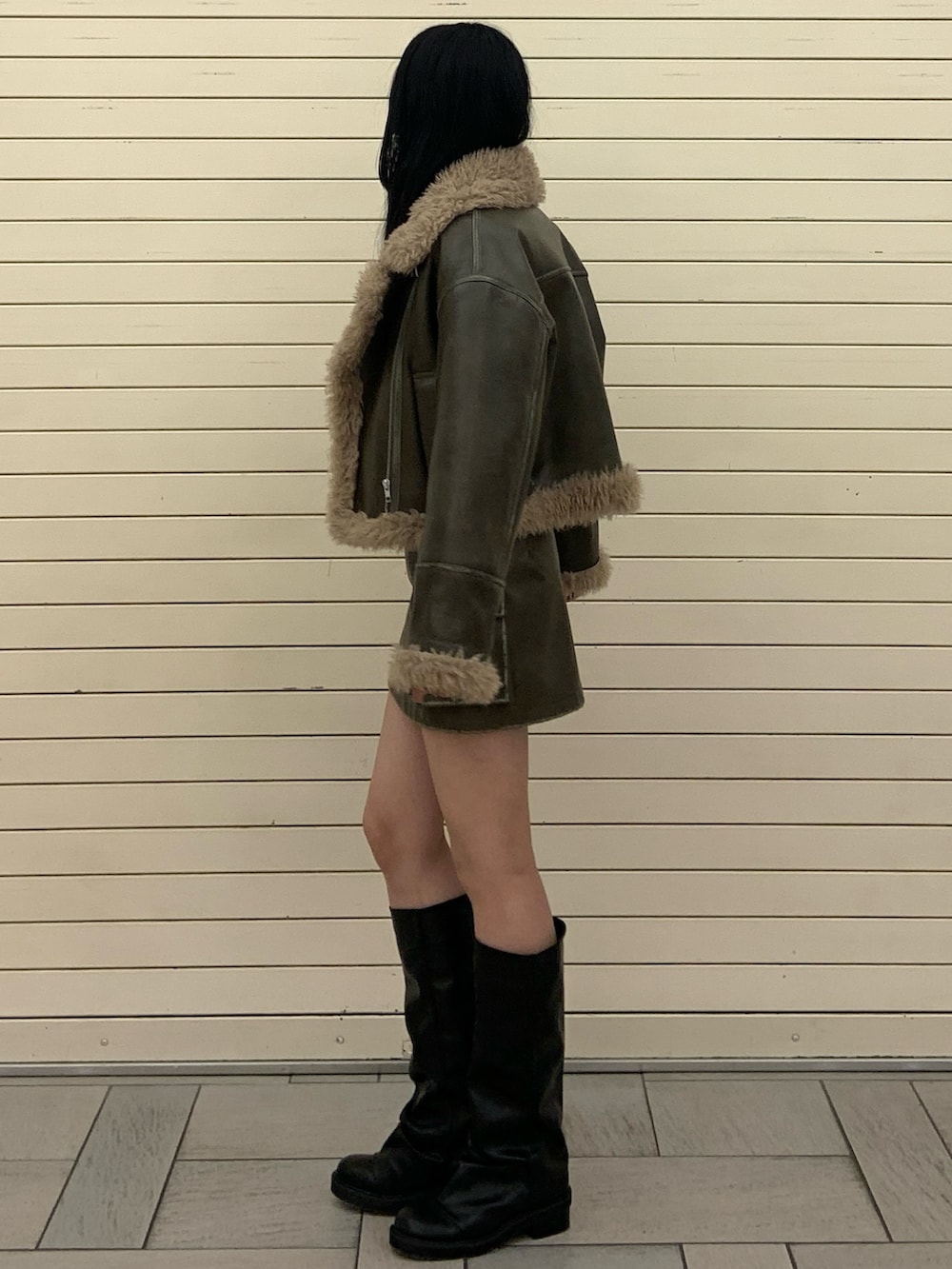 グリーン系のムートンコート、ブラック系のニット/セーター、グリーン系のスカートを着用したレディースの冬コーディネートの3枚目の写真