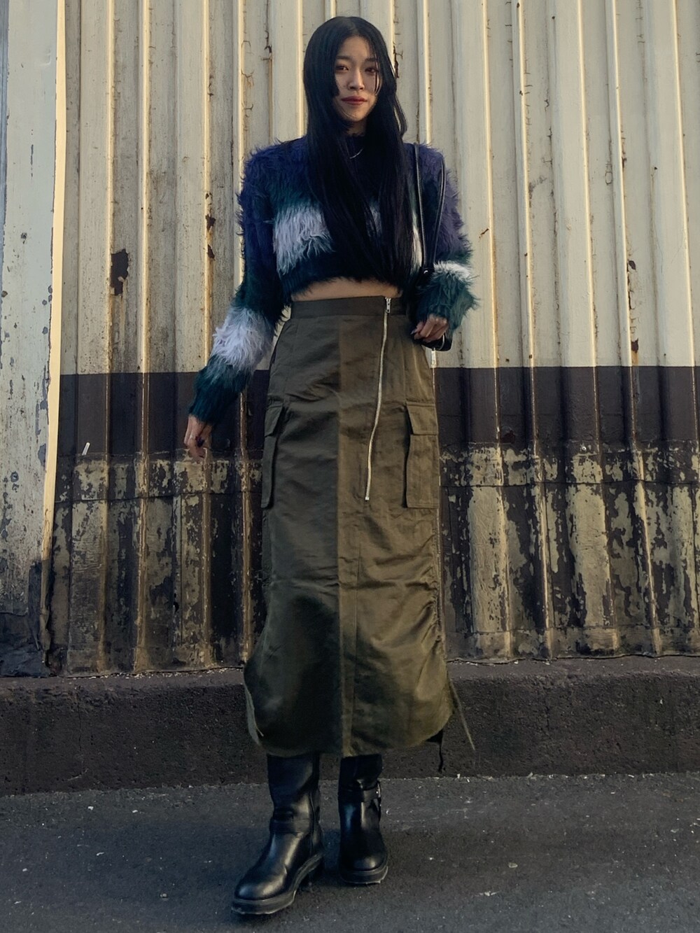 ブルー系のニット/セーター、ブラック系のボストンバッグ、グリーン系のスカートを着用したレディースの冬コーディネートの2枚目の写真