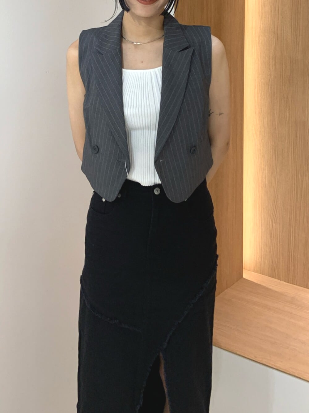 グレー系のベスト、ブラック系のサンダル、ブラック系のデニムスカートを着用したレディースの夏コーディネートの4枚目の写真